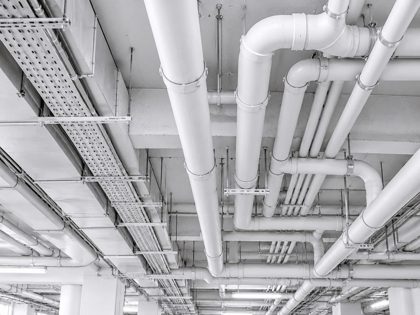 Overhead plumbing pipework, drainage stacks and cable trays suspended beneath a concrete slab